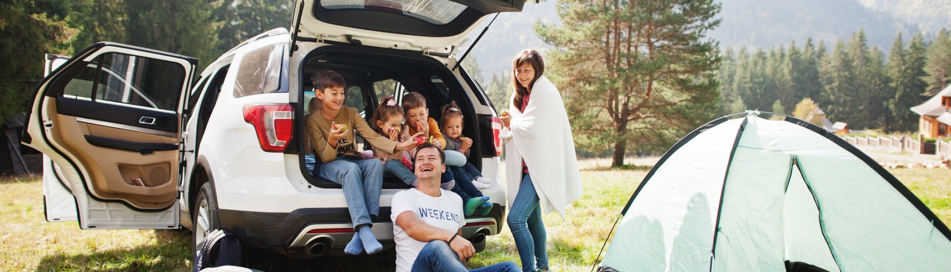 Family sitting around white chevrolet suv, next to tent.